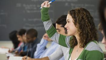 Ung kvinnelig student rekker opp hånda i et klasserom