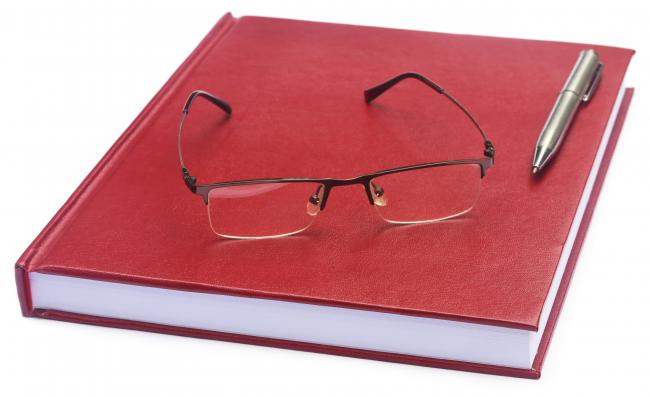 Bilde av rød bok med briller og en penn.