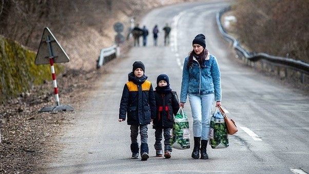 Bilde av mor og barn med poser med klær som går langs en øde vei.