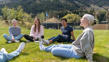 Bilde viser studenter som sitter i ring på en gressplen og prater og ler