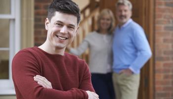 Bilde av smilende ung mann med foreldre i bakgrunnen