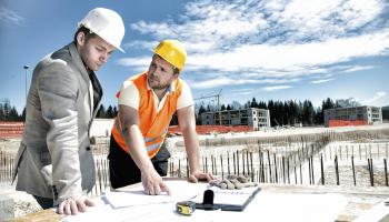 To bygningsarbeidere står bøyd over et bord på en byggeplass.