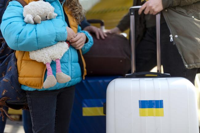 Bilde av barn med bamse og kofferter med ukrainske flagg.