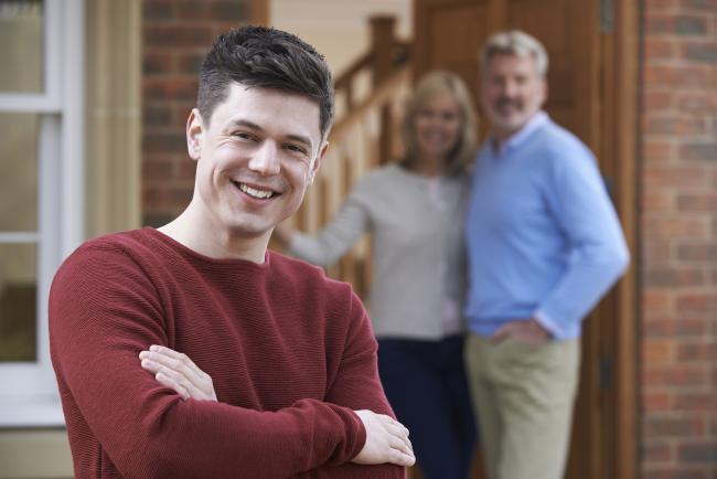 Bilde av smilende ung mann med foreldre i bakgrunnen