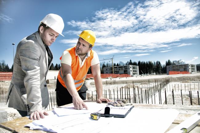 To bygningsarbeidere står bøyd over et bord på en byggeplass.
